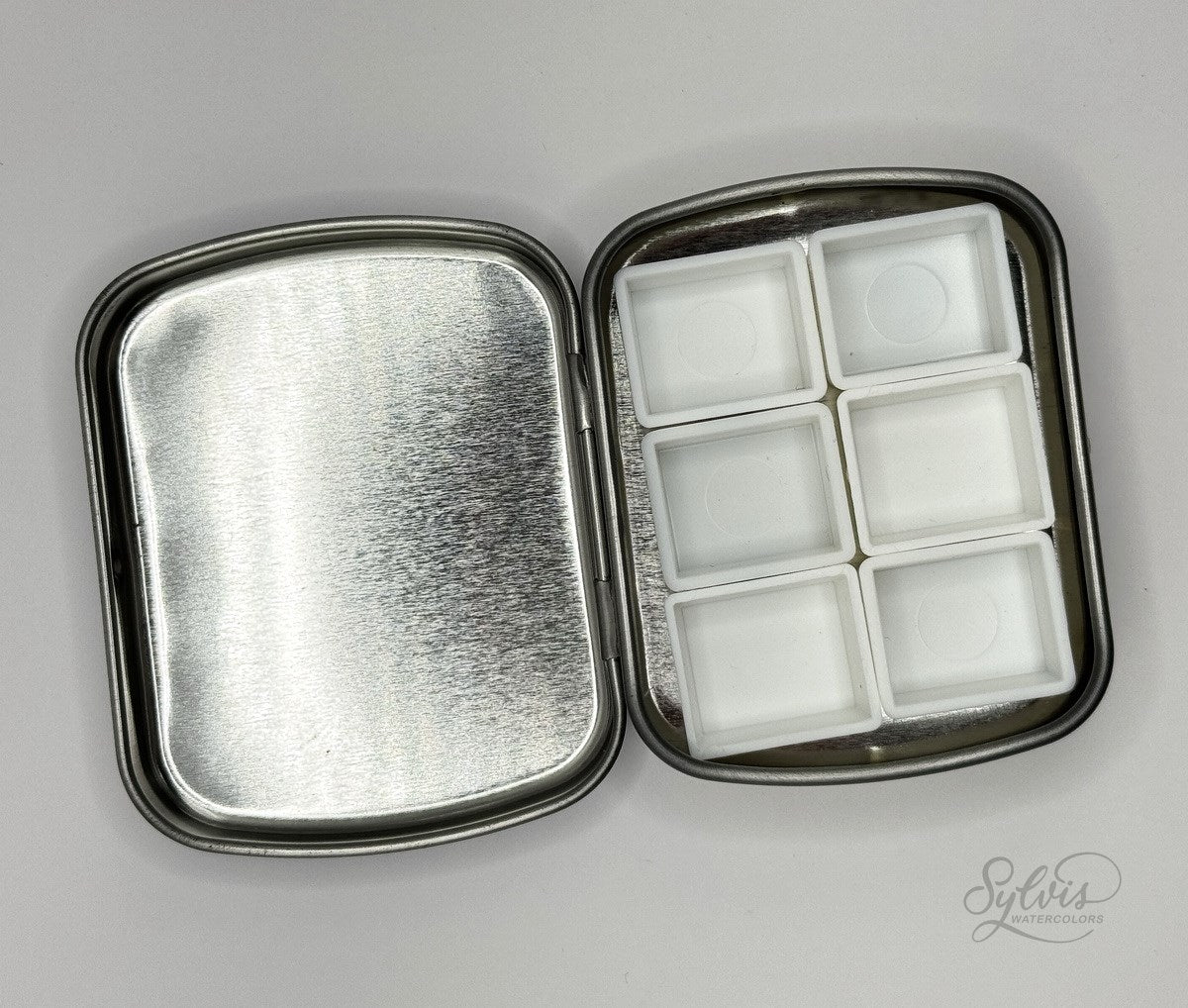 Kleine Weißblechdose, geöffnet mit 6 halben leeren Näpfchen im Unterteil zur Platzdemonstration