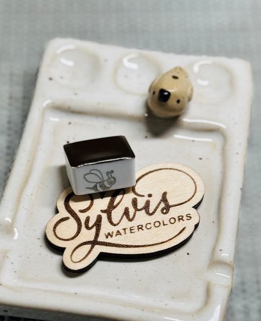 Handgemachte Aquarellfarbe Indian Yellow Imitation im halben Näpfchen, darunter Holzlogo Sylvis Watercolors auf Steingutpalette mit kleinem Vöglein – Künstlerqualität aus dem Hochsauerland