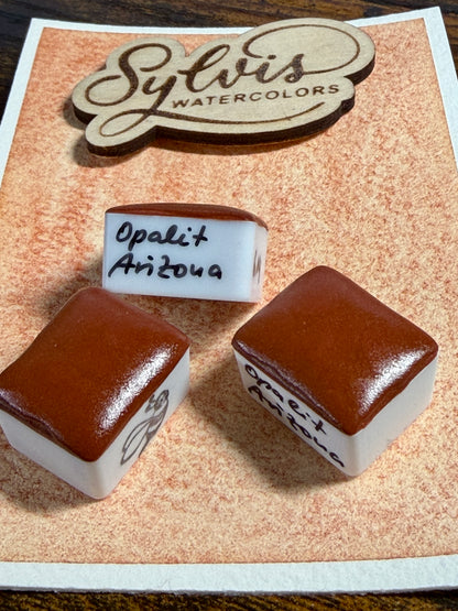 halbe Näpfchen mit roter Opalit aus Arizona auf Farbswatch auf Aquarellpapier dekoriert, im Hintergrun Logo aus Holz SylvisWatercolors