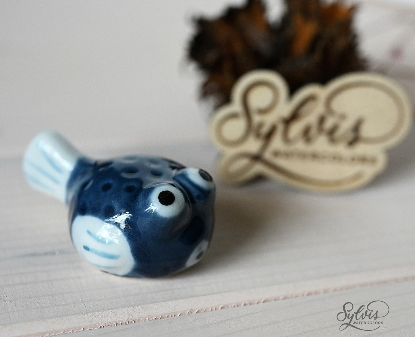 blau-weißer Kugelfisch aus glasierter Keramik als Pinselablage, im Hintergrund Logo aus Holz, Deko